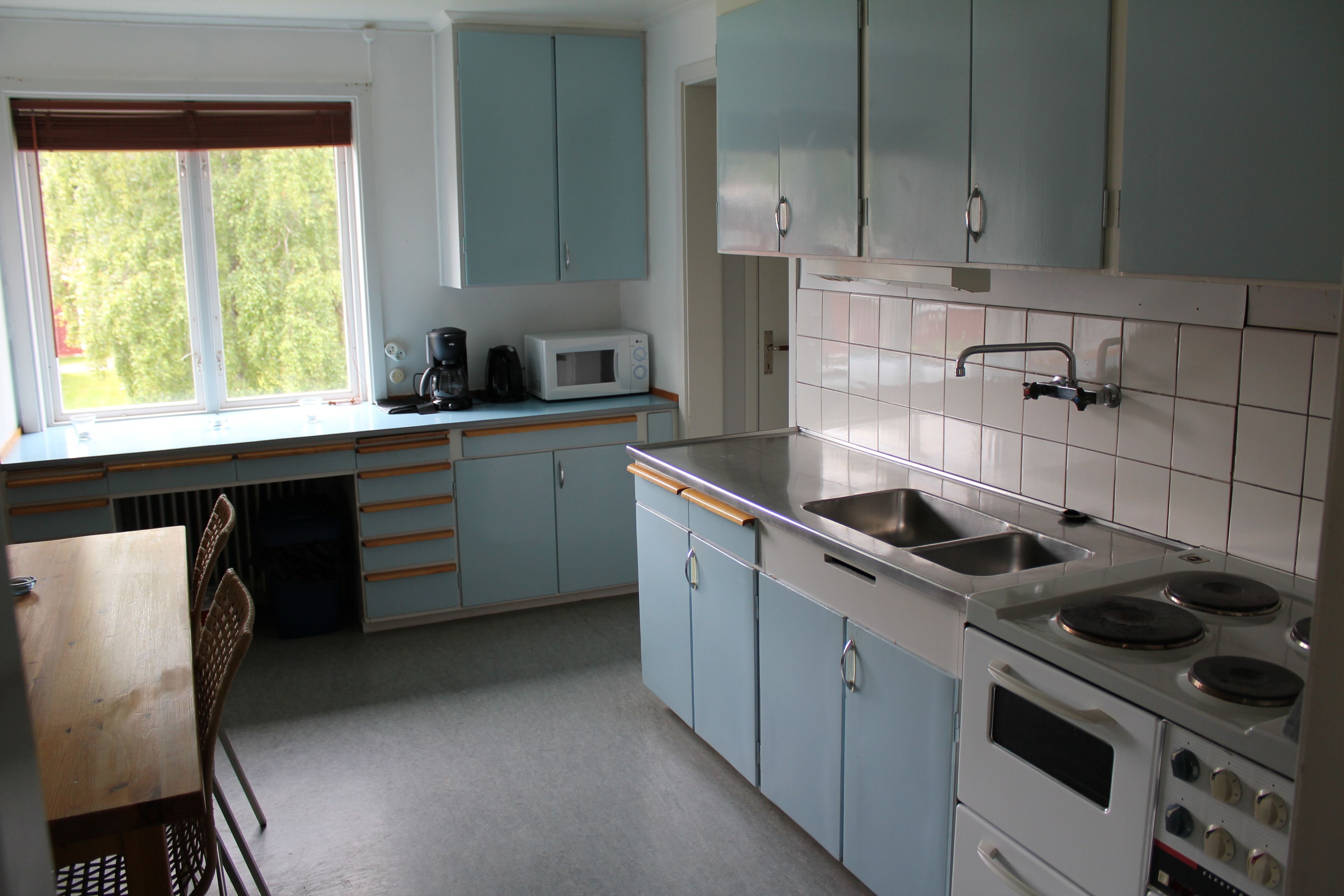 A kitchen with light blue cabinets, a white stove, a sink, and a window with blinds.