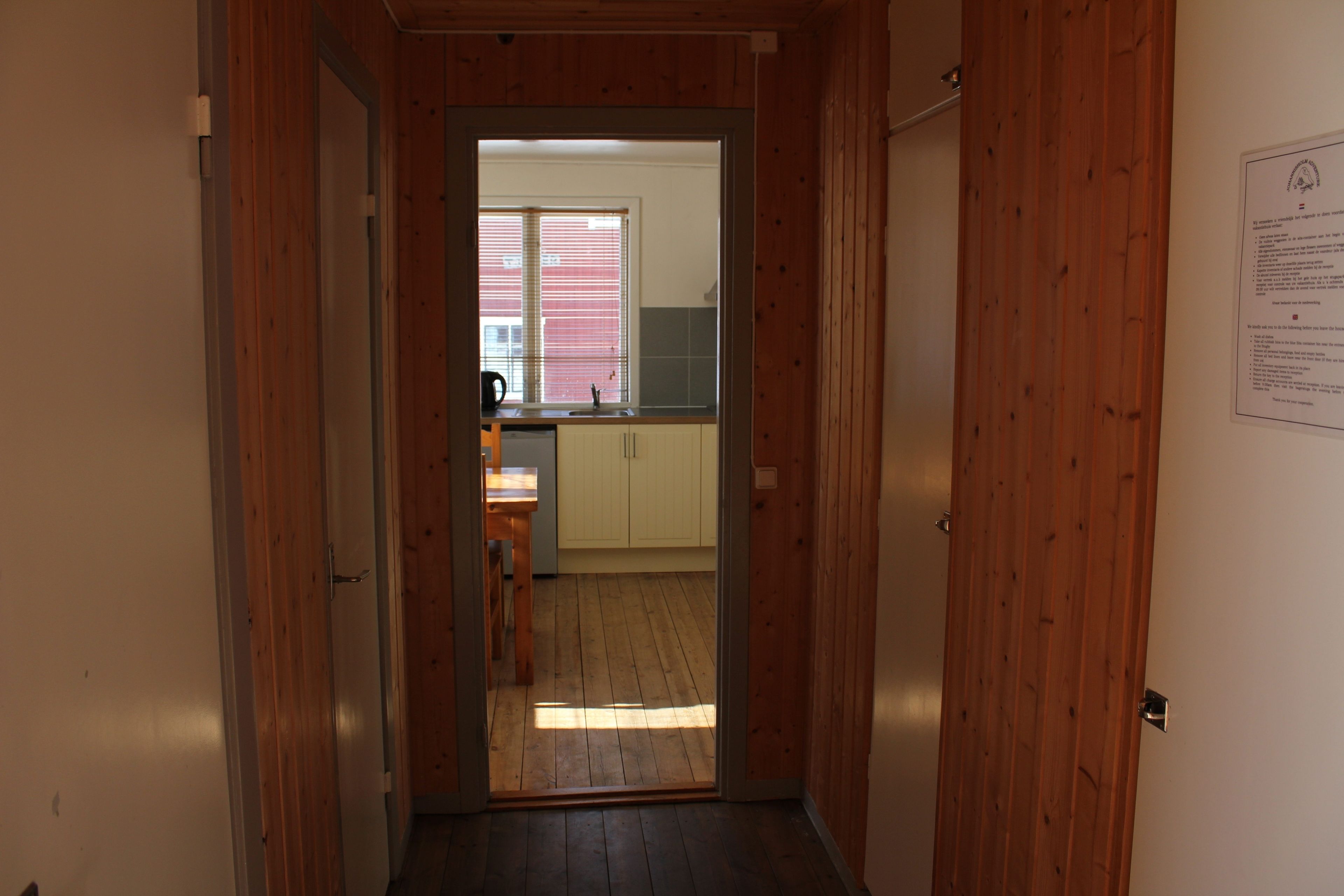 A hallway leading to a kitchen with wooden walls and a window with blinds.