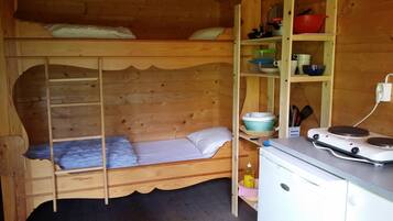 Una cabaña de madera con literas, una kitchenette con estufa y repisas con utensilios de cocina.
