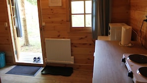 Interior de una cabaña de madera con puerta y ventana de madera, un radiador, un microondas y una estufa.