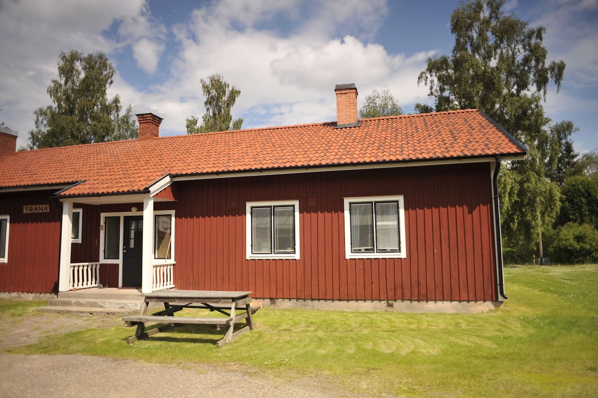 A red wooden building with a tiled roof, a front porch, and a picnic table.