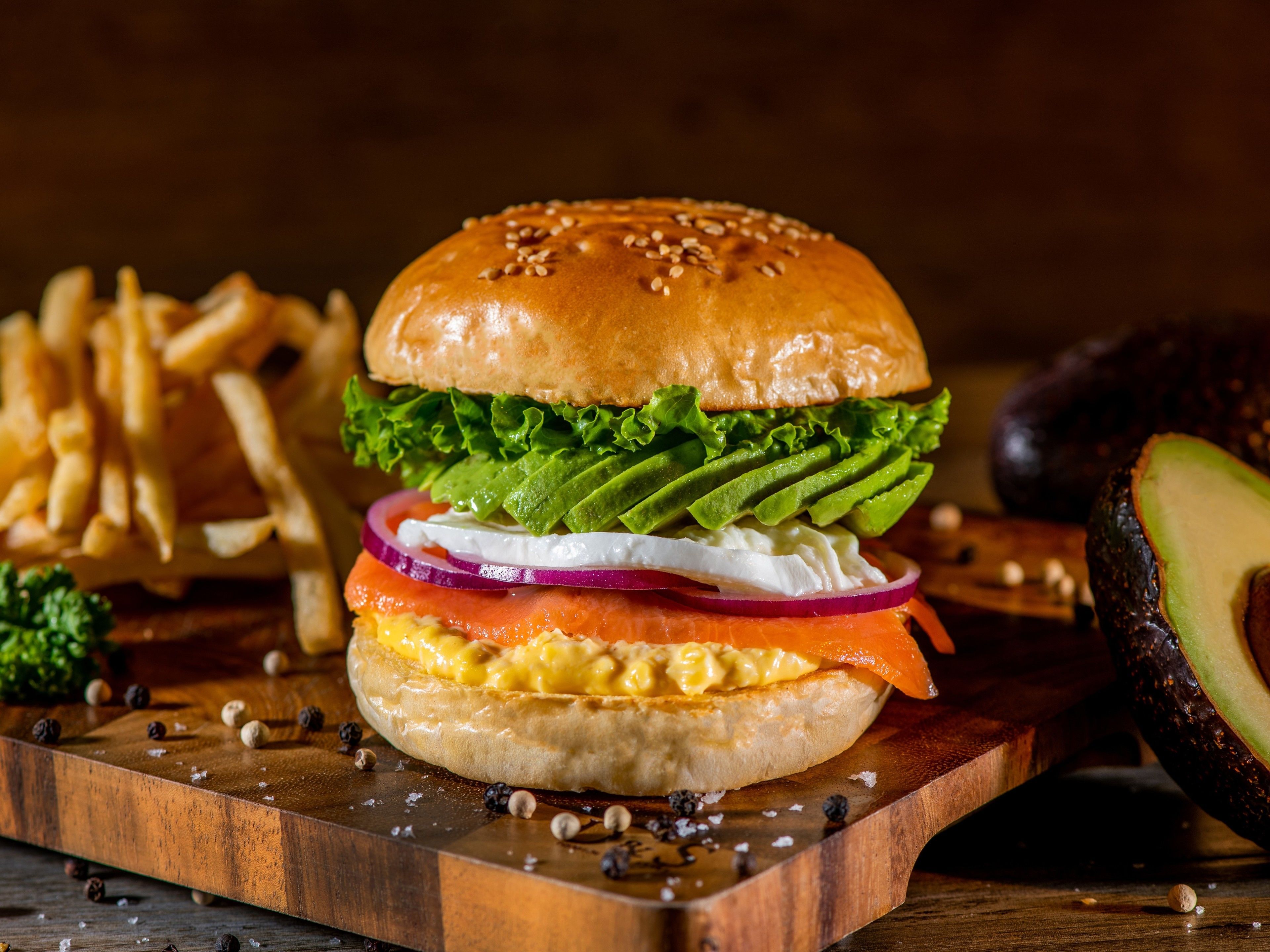 A sandwich with lettuce, tomato, and cheese on a bun, accompanied by fries and an avocado.