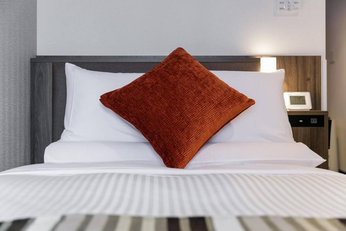 A neatly made bed with white bedding and a single brown pillow.
