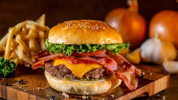 Un hamburger garni de laitue, de fromage et de bacon, servi dans un pain, accompagné de frites et d’oignons sur une planche en bois.
