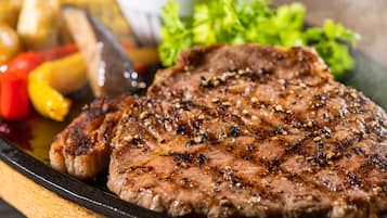 A grilled steak with vegetables and a small bowl of sauce.