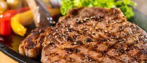 Un bistec a la parrilla con verduras y un recipiente pequeño con salsa.
