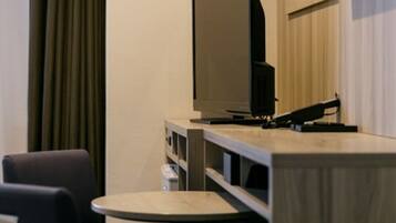 A hotel room with a flat-screen TV on a wooden stand, a small round table, and a sofa.
