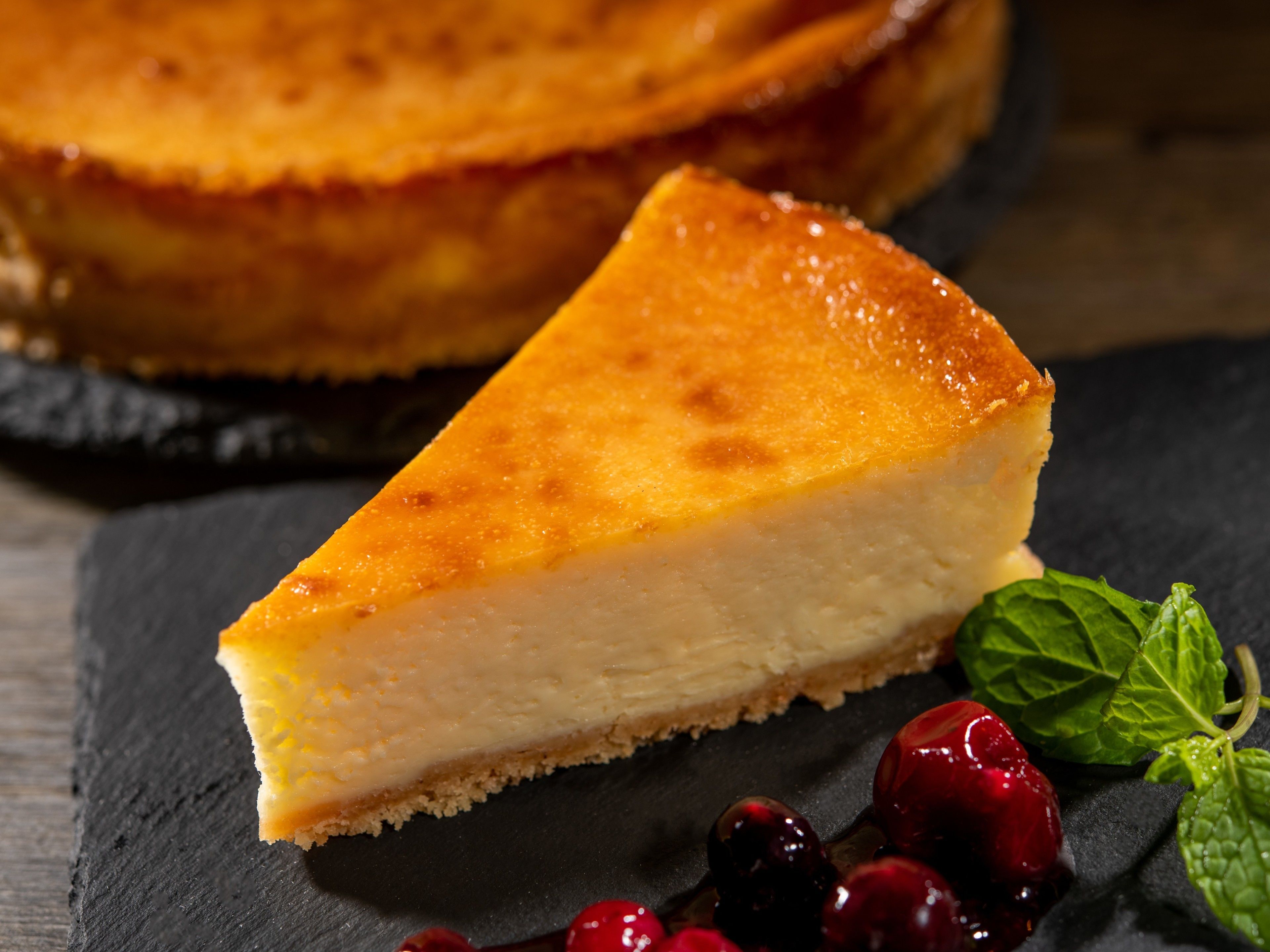 A slice of cheesecake on a slate plate with cranberries and mint leaves.