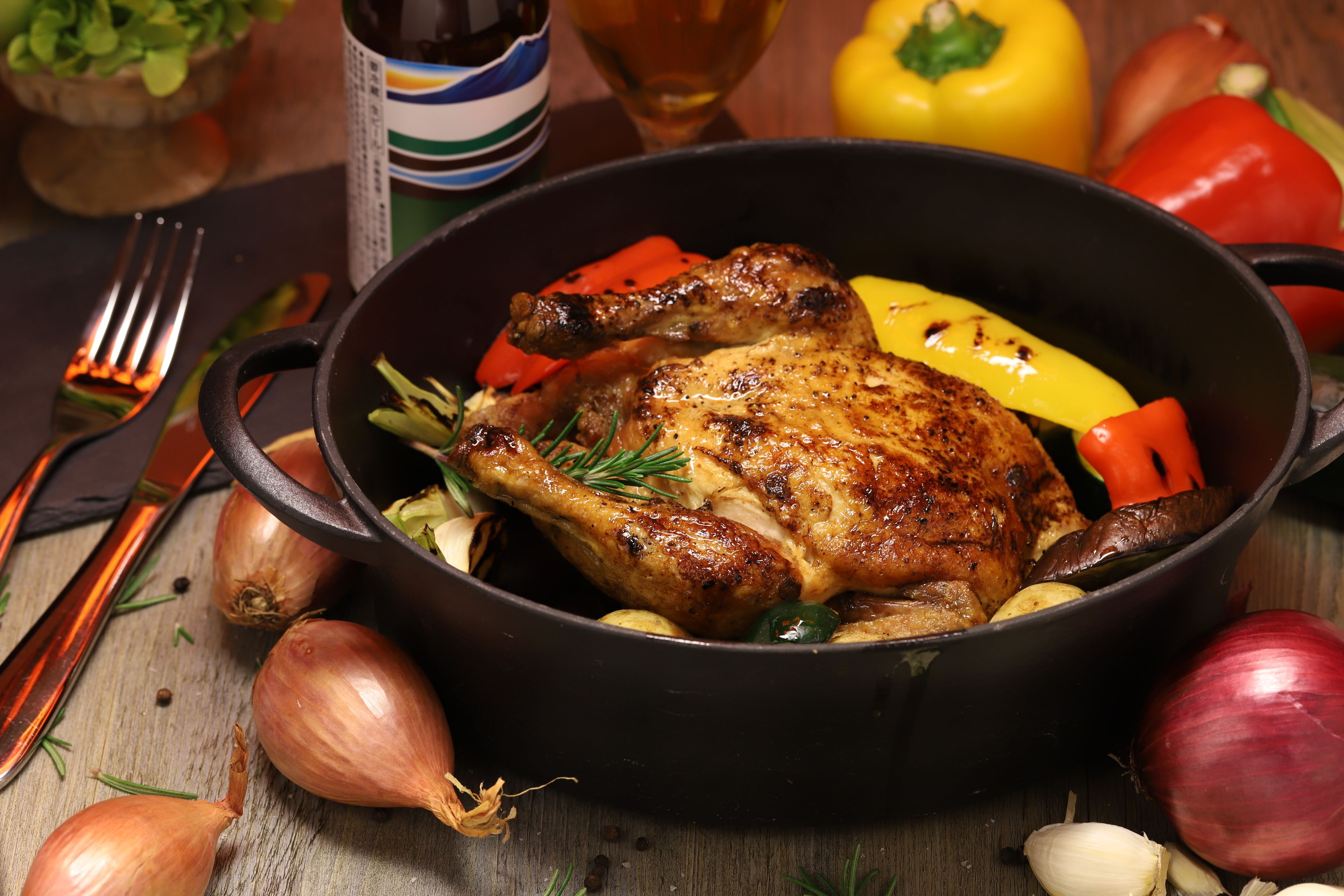 Un pollo asado en una sartén de hierro fundido rodeado de verduras y especias.