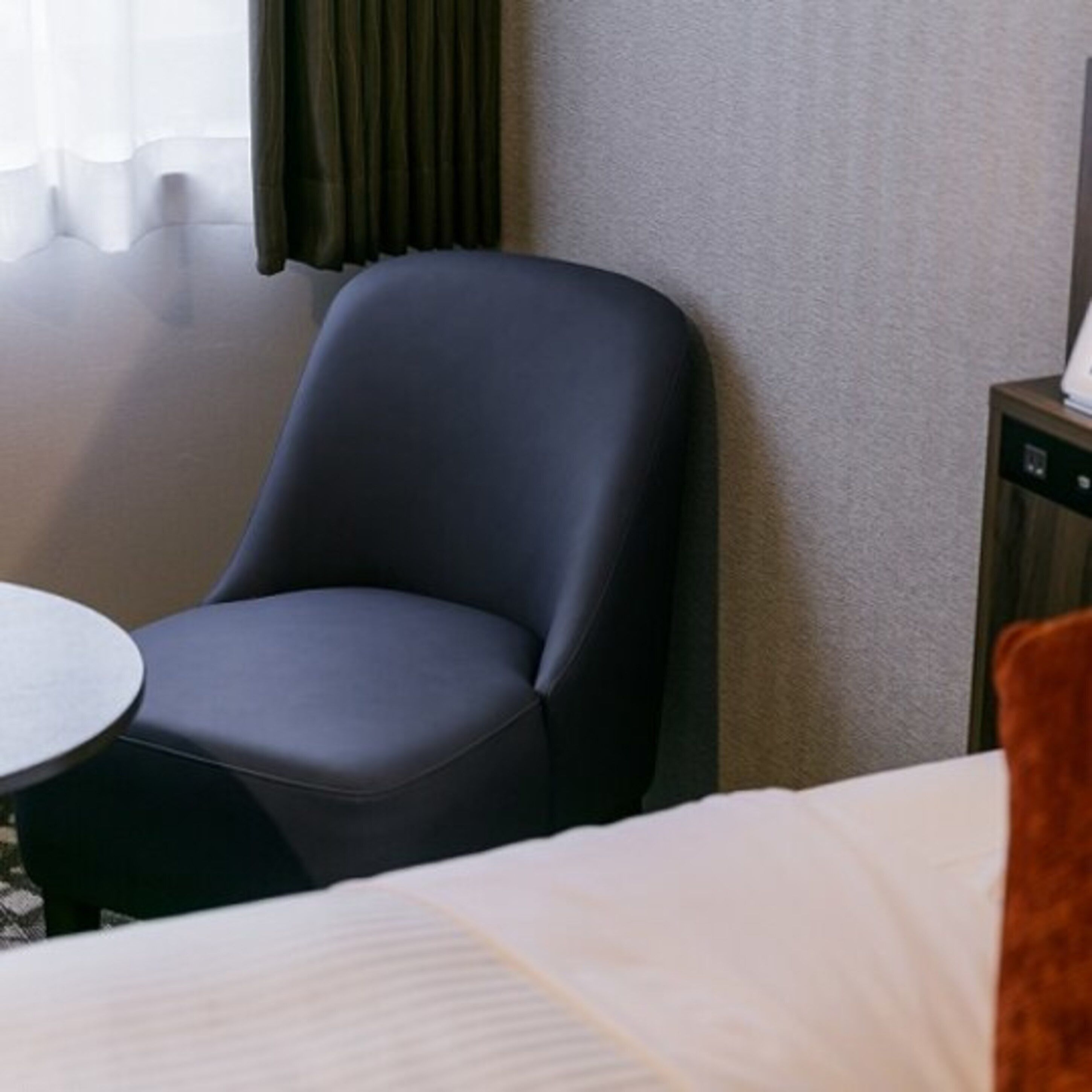 Una habitación de hotel con una cama, una silla, una mesita y un dispositivo fijado a la pared.