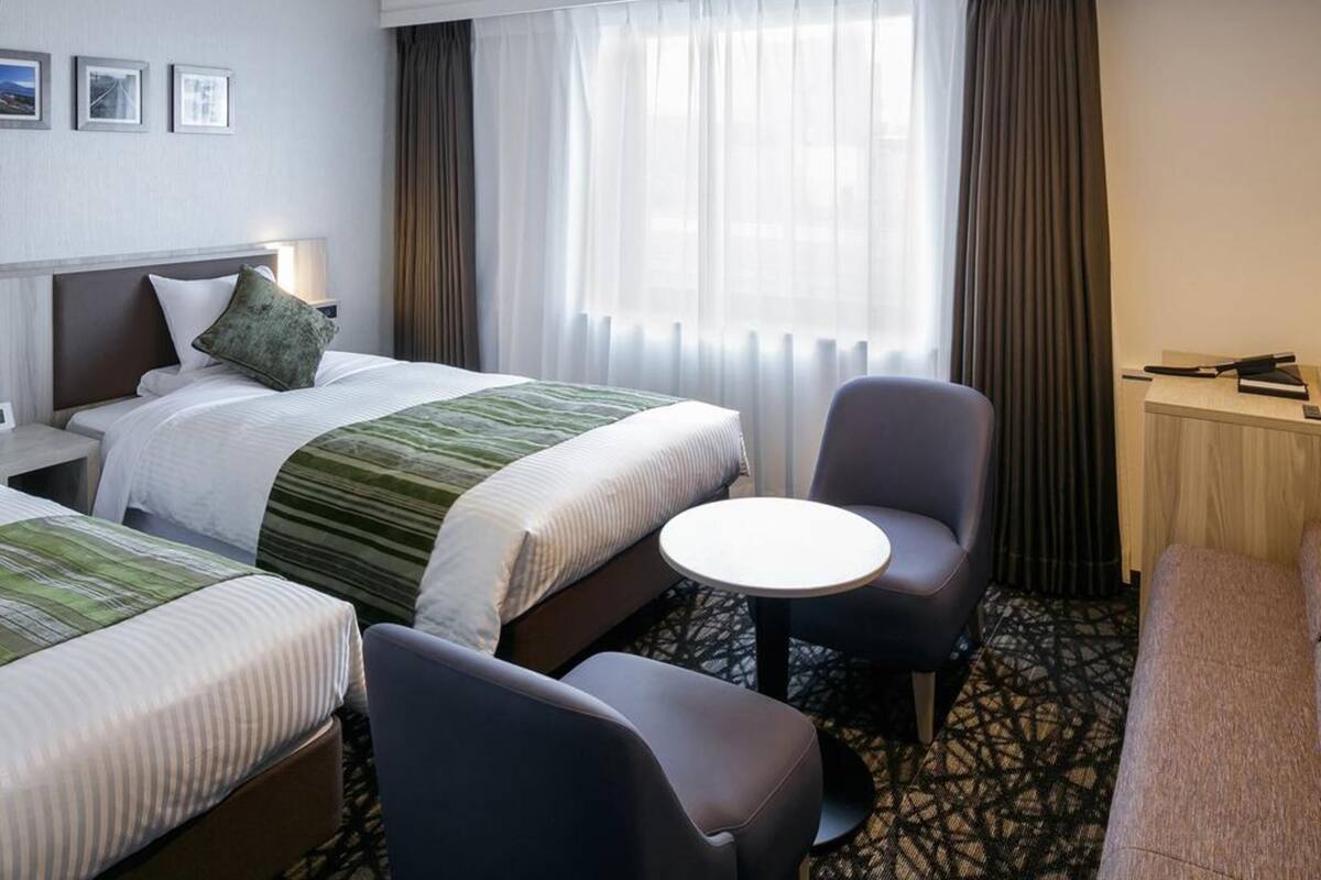 A hotel room with two beds, a desk, a chair, and a small table.