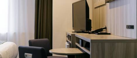 A hotel room with a bed, a desk with a computer, a chair, and a TV.