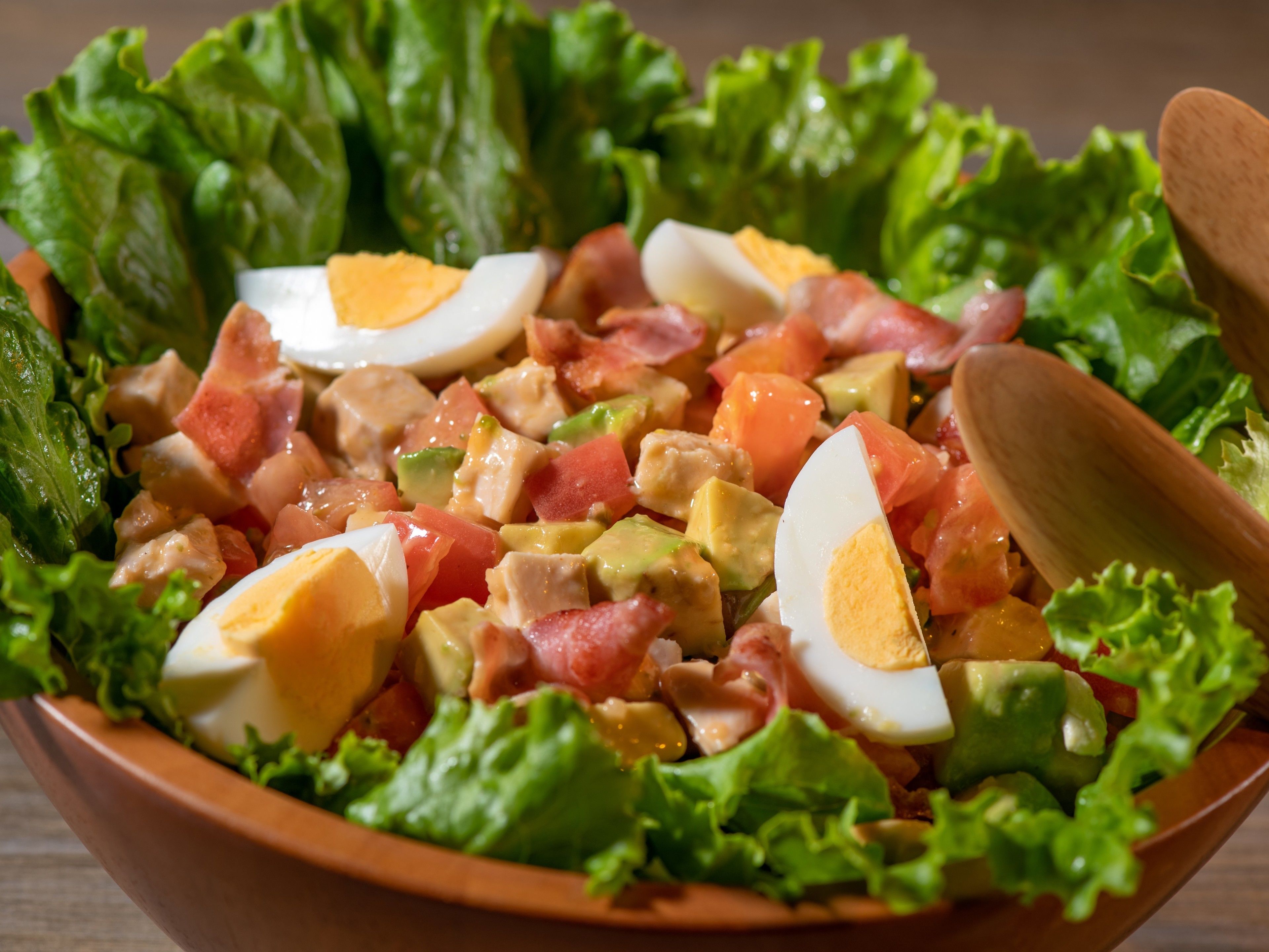 A bowl of salad with lettuce, tomatoes, avocado, and hard-boiled eggs.