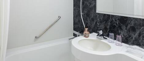 Een badkamer met een wit bad, een wastafel met een marmeren achterwand en een spiegel boven de wastafel.