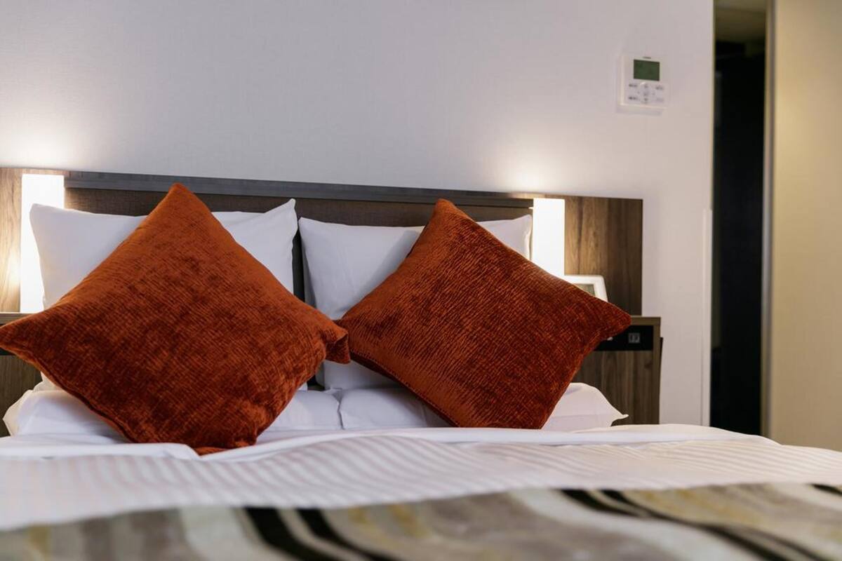 A neatly made bed with white linens and two large orange pillows.