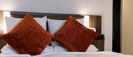 A neatly made bed with white linens and two large orange pillows.