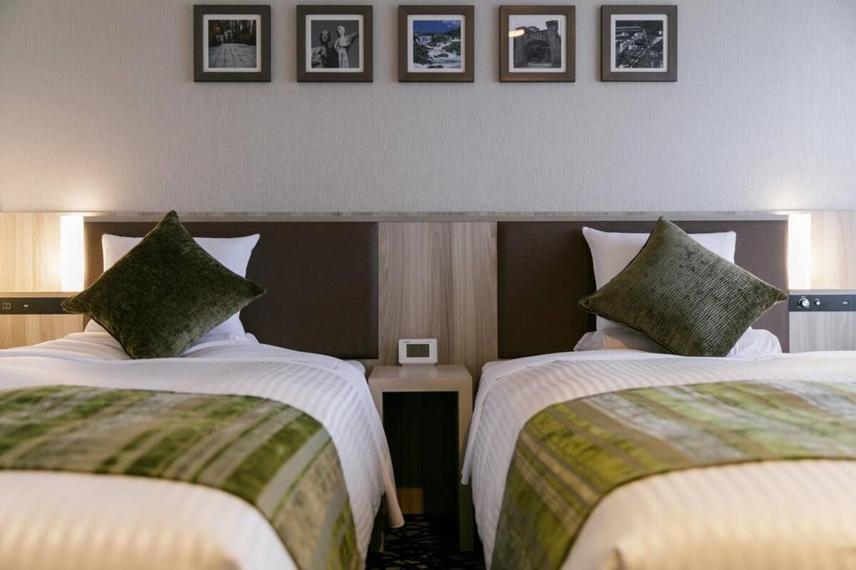 A hotel room with two beds, a nightstand between them, and a wall-mounted clock.