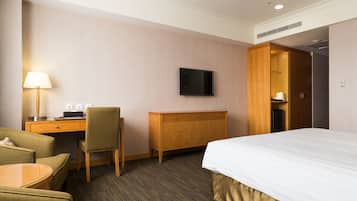Habitación de hotel con cama, escritorio, silla, televisor y armario.