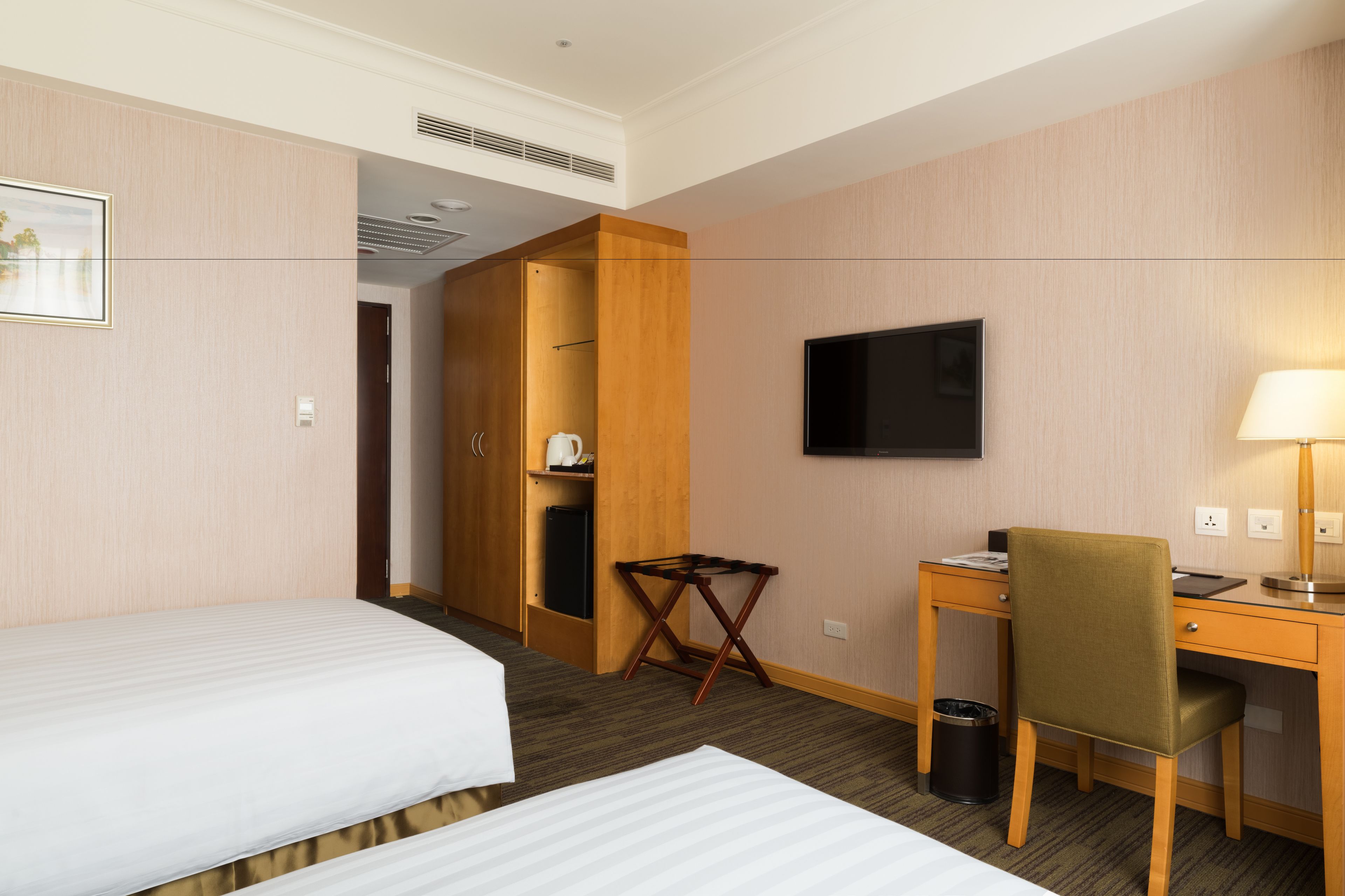 A hotel room with two beds, a desk, a chair, a television, and a small table.