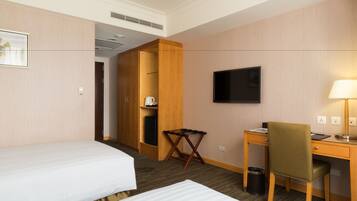 A hotel room with two beds, a desk, a chair, a television, and a small table.
