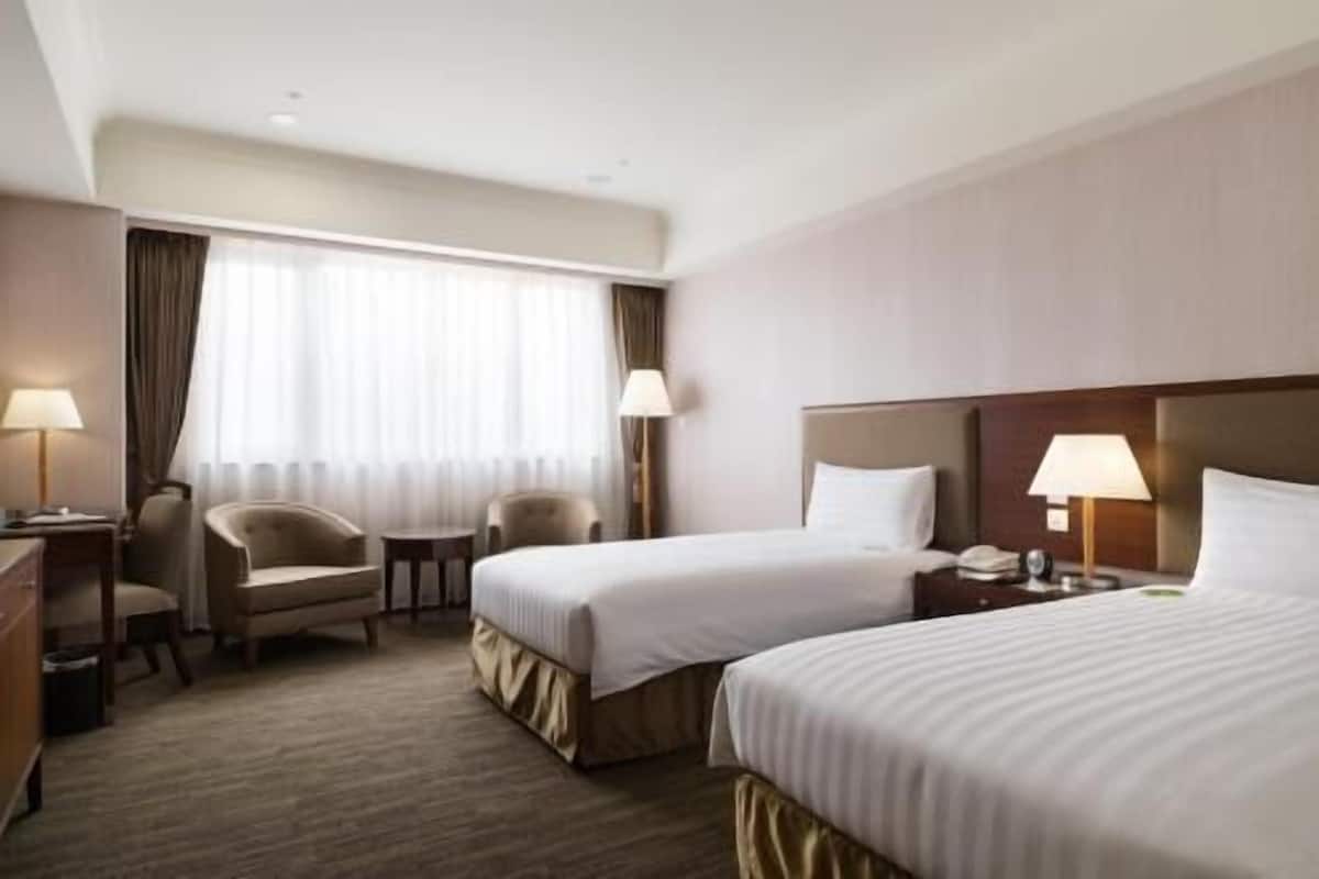 Habitación de hotel con dos camas, un escritorio, una silla y una ventana con cortinas.