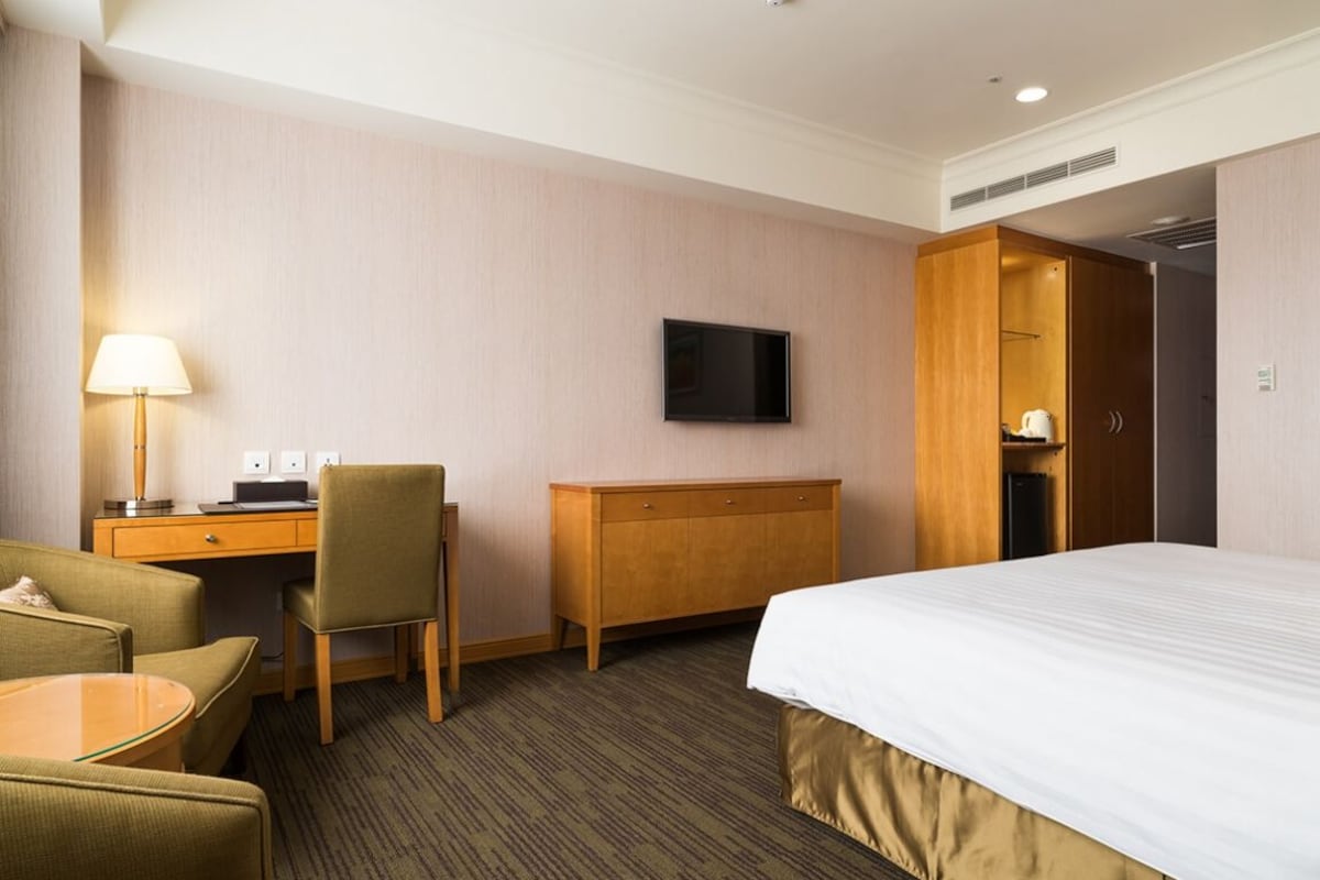 Een hotelkamer met een bed, bureau, stoel, televisie en kledingkast.