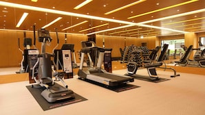 Ein Fitnessraum mit verschiedenen Cardiogeräten, darunter Laufbänder und Crosstrainer, in einem großzügigen Bereich mit Holzvertäfelung und moderner Beleuchtung.
