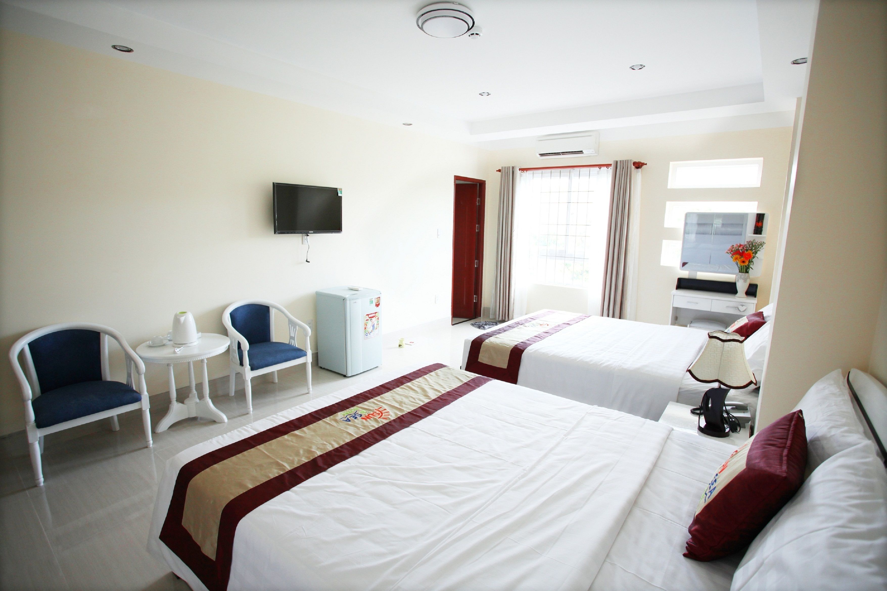Habitación de hotel con dos camas, televisión, una mesita, dos sillas y ventana con cortinas.