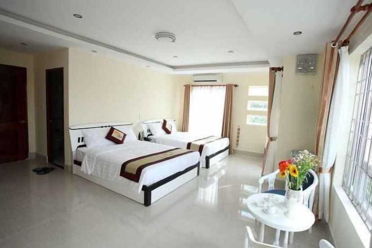 A hotel room with two beds, a small table, and a window with curtains.