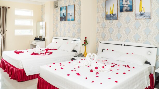 A hotel room with two beds, a vase with flowers, and nautical-themed wall art.