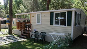 A mobile home with a deck, two chairs, and a small table.