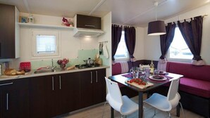 A compact kitchen with dark cabinets, a white countertop, and a dining area with a table and chairs.