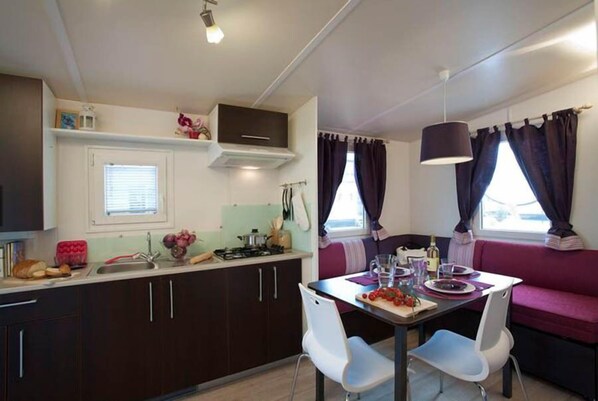 A compact kitchen with dark cabinets, a white countertop, and a dining area with a table and chairs.