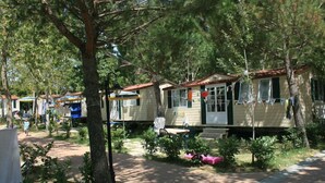 A row of mobile homes with attached porches, surrounded by trees and greenery.