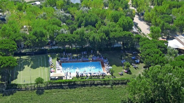 An aerial view of a resort with a swimming pool, tennis courts, and lush greenery.
