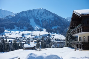 A snow-covered mountain village with traditional wooden buildings, a ski slope, and a clear blue sky.
