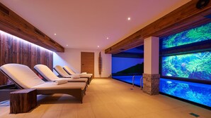 A spa area with wooden paneling, a large aquarium, and several lounge chairs. - Boutique Hotel Herzhof Garni - Apartments (Mittelberg)