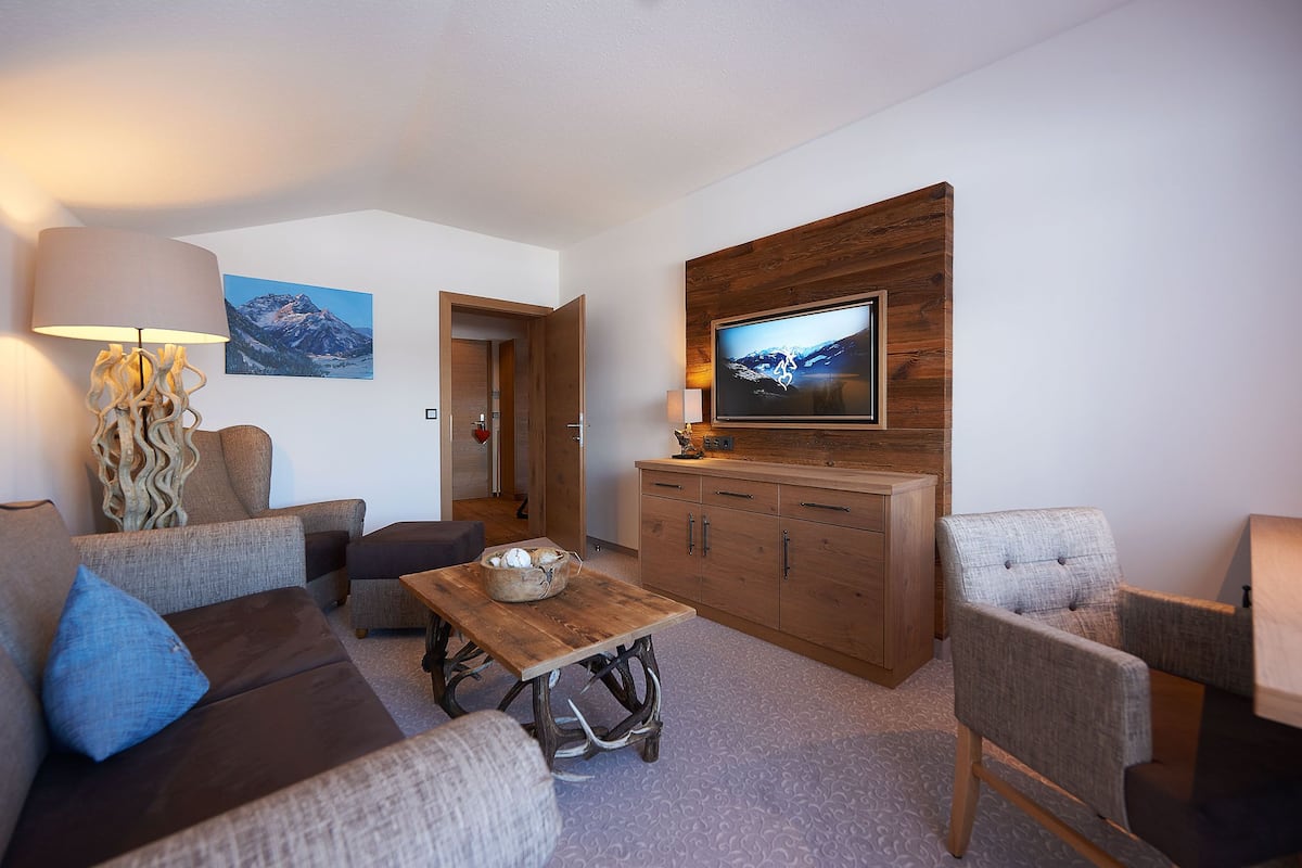 En moderne stue med sofa, lænestole, et træsofabord og et fjernsyn monteret på en væg af træpaneler.