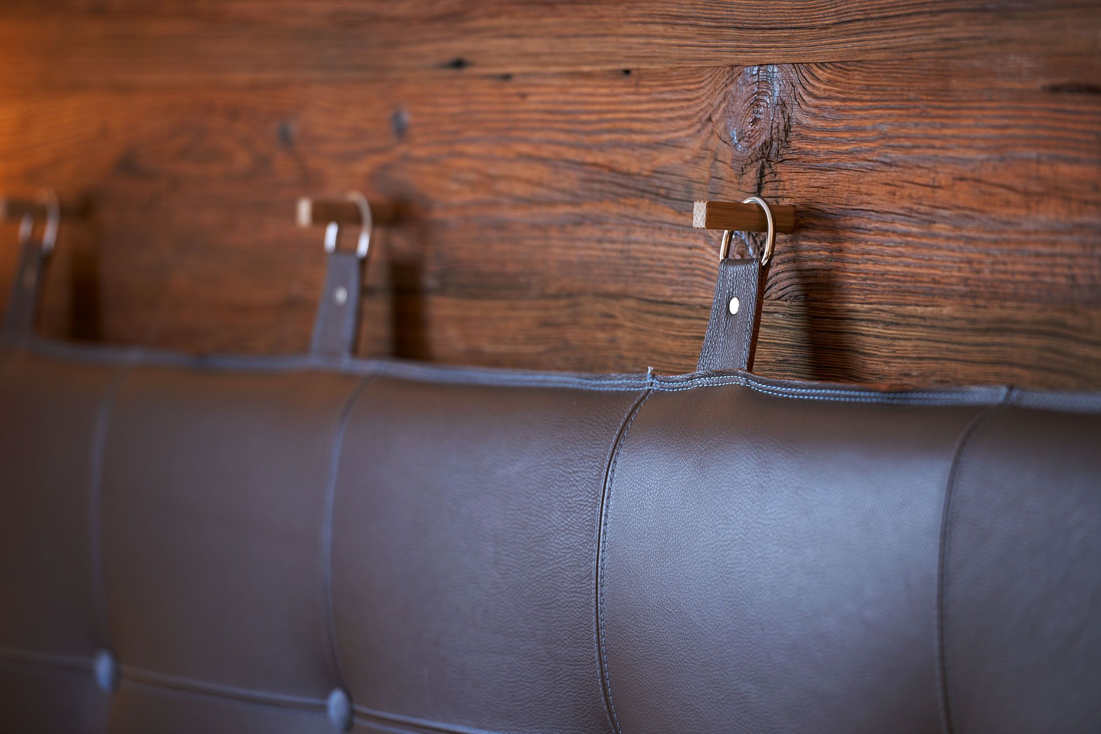 A close-up of a leather couch with metal clips attached to a wooden wall.