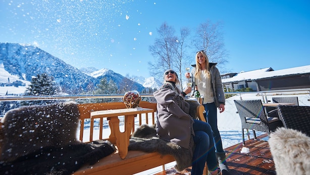 A snowy outdoor deck with a wooden bench, a wicker chair, and a table. - Boutique Hotel Herzhof Garni - Apartments (Mittelberg)