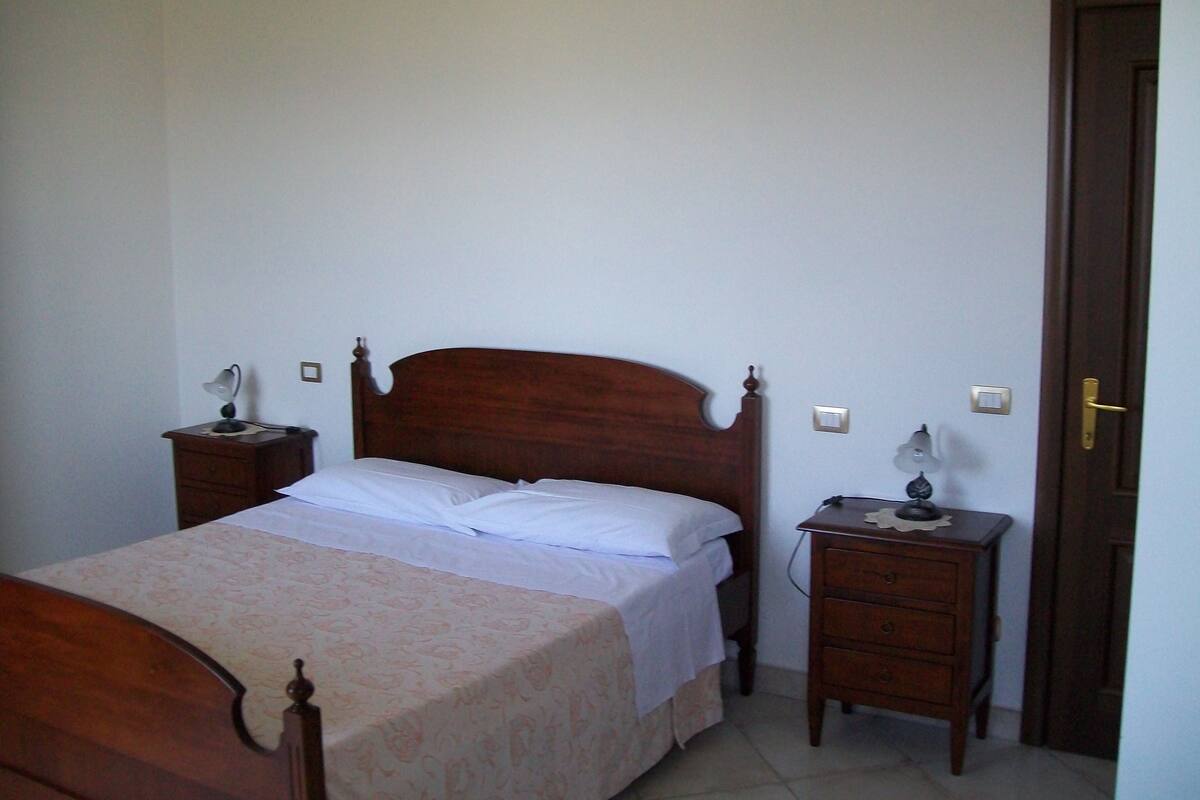 Ein Schlafzimmer mit einem hölzernen Bett, Nachttischen und einer Tür.