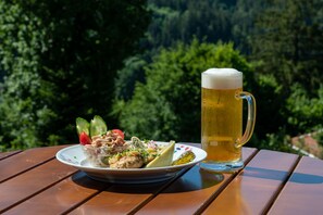 A meal with a beer mug on a wooden table outdoors with a forest backdrop.