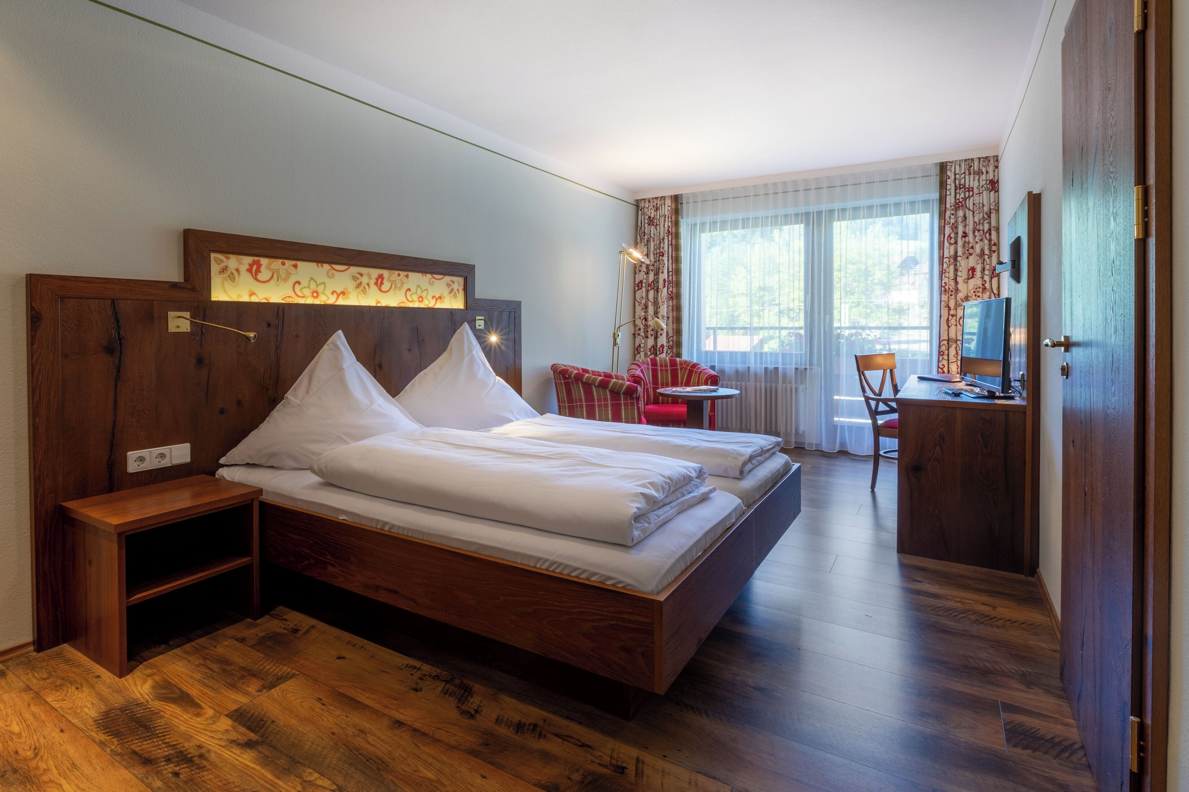 A hotel room with a wooden bed, a desk, a chair, and a small table.