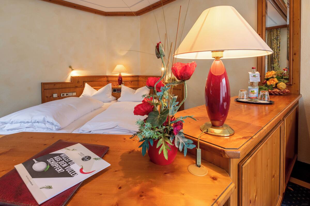 Quarto de hotel com cabeceira de madeira, mesa de cabeceira com abajur, um vaso com flores e um menu na mesa.
