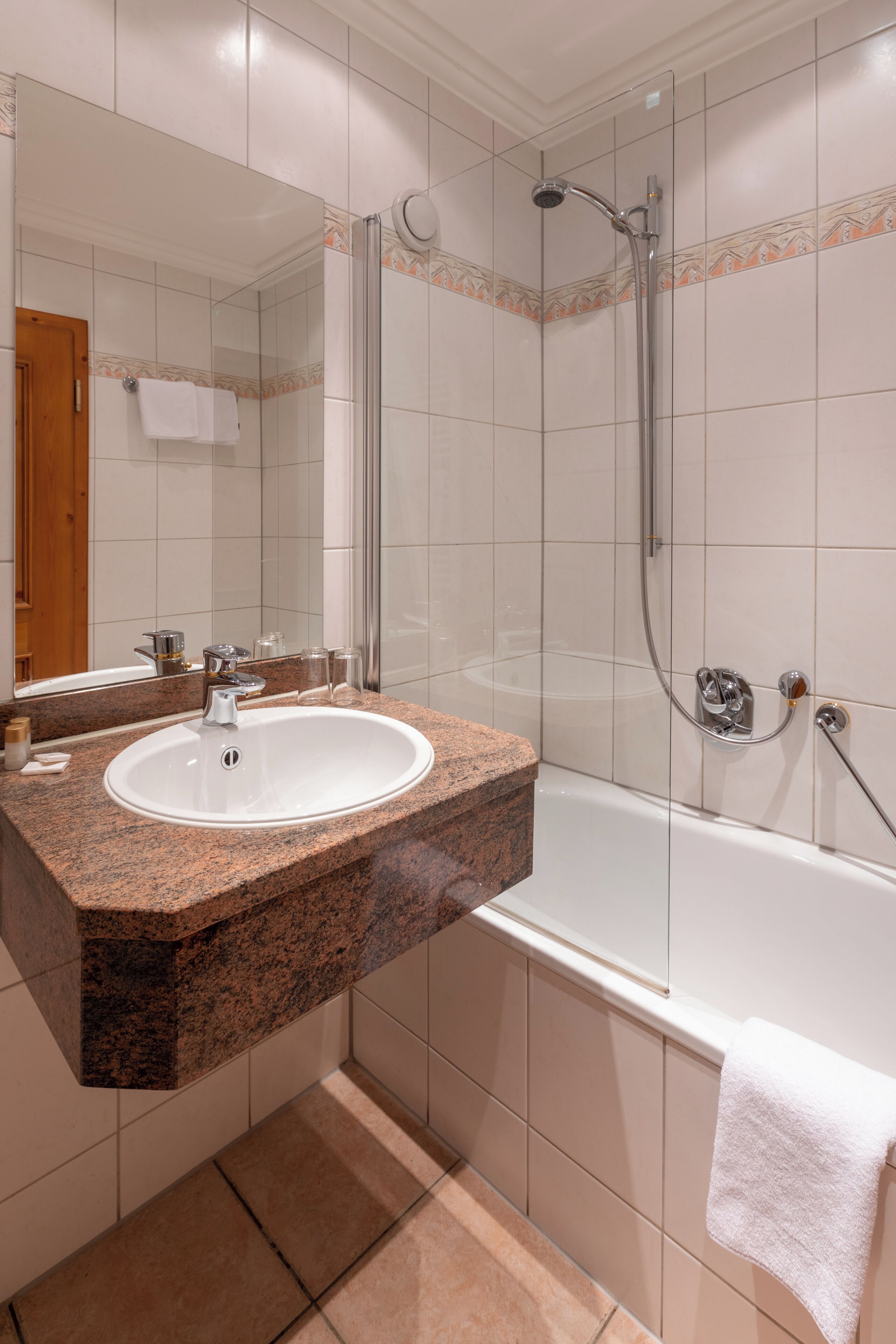 Un baño con lavamanos de encimera de granito, ducha con cerramiento de vidrio y bañera blanca.