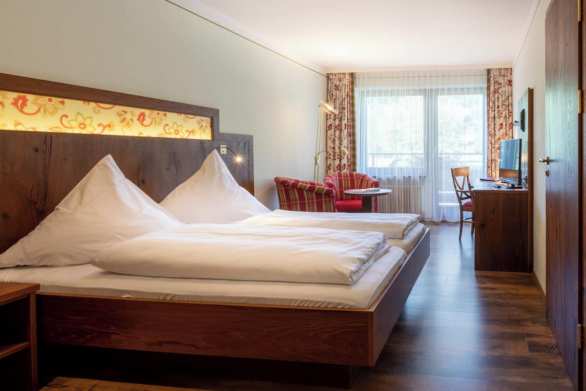 Quarto de hotel com duas camas, uma escrivaninha, uma cadeira e uma televisão.