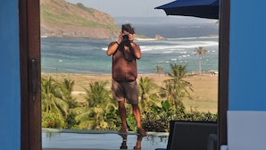 A man taking a photo of the ocean from a balcony with a view of the beach and palm trees. - Blue Monkey Villas Resort & Ocean View (Kuta)