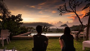 Two people sitting on a patio overlooking a body of water with a sunset view. - Blue Monkey Villas Resort & Ocean View (Kuta)