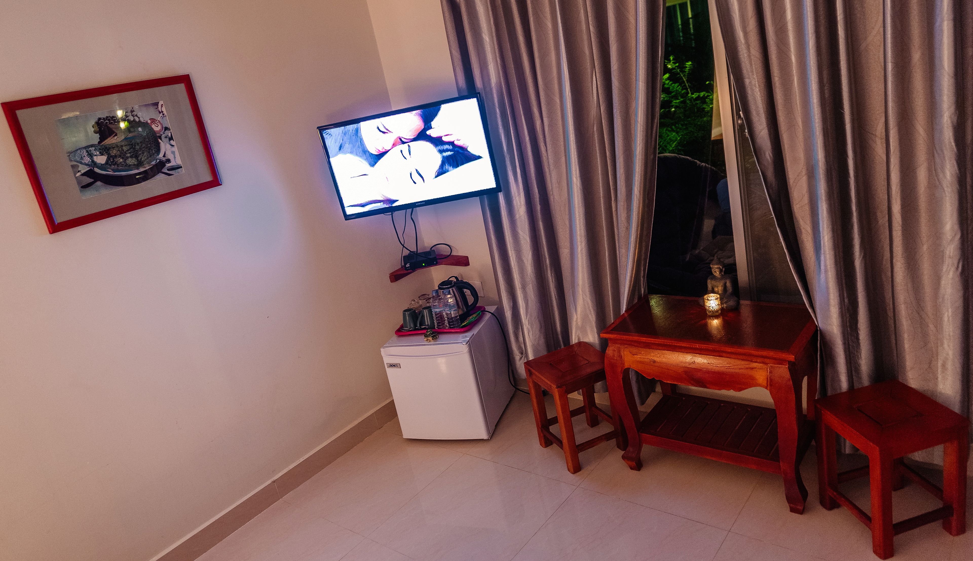 Une petite pièce avec un téléviseur, un réfrigérateur, une table et une chaise.