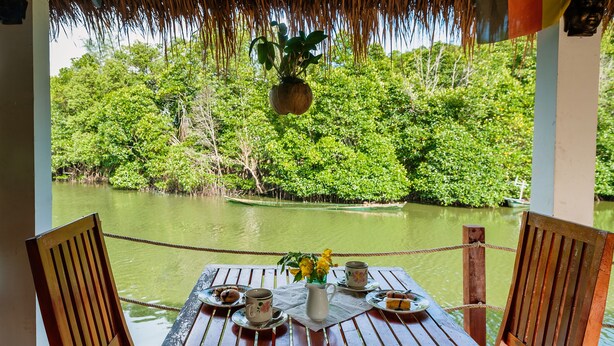 A wooden table with plates, cups, and a pitcher, set against a backdrop of a river and lush greenery. - Spayhiti (Sihanoukville)